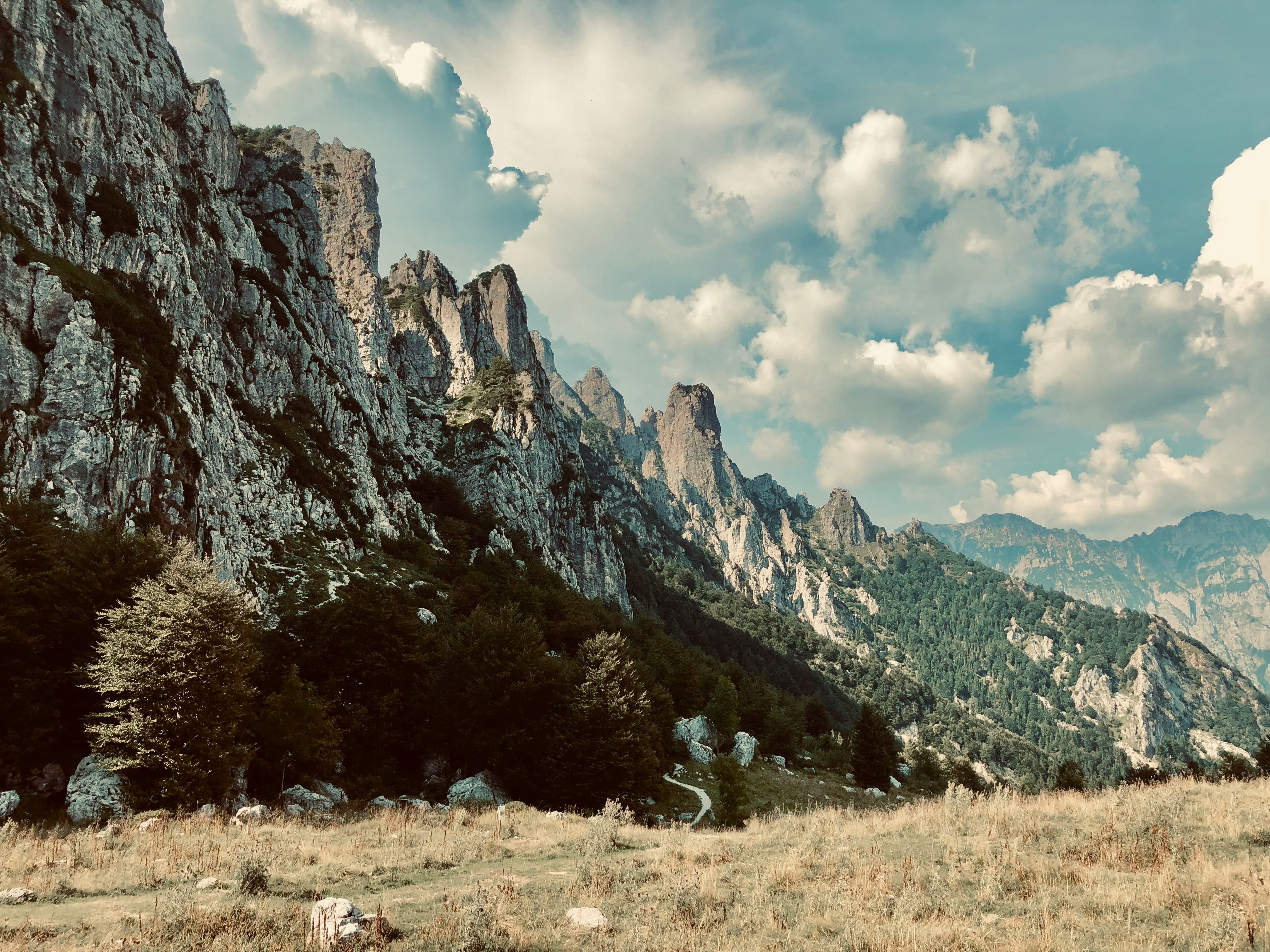 green grass field near rocky mountain under white clouds during daytime